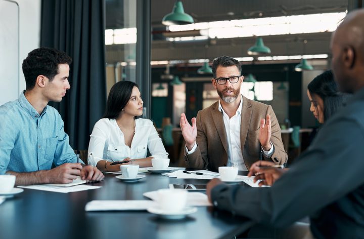 People sat around a table in a meeting, with one person leading the conversation