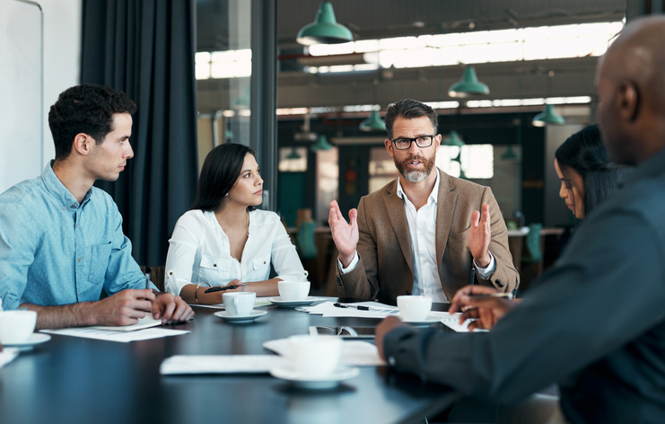 People sat around a table in a meeting, with one person leading the conversation